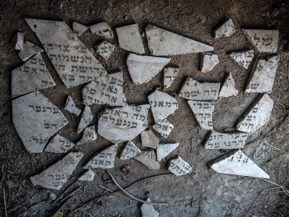 Fragmente von Grabsteinen, schwarz-weiss, auf dem Boden liegend.