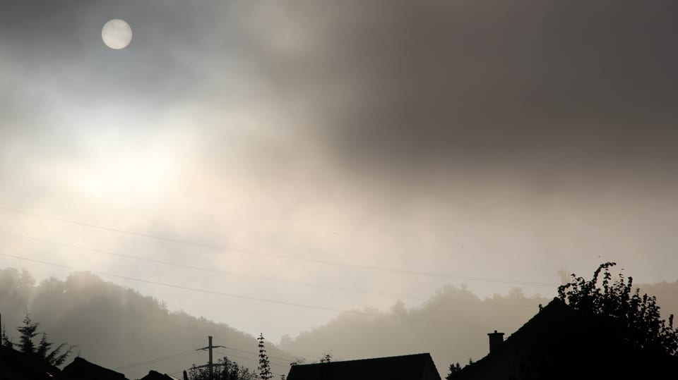 Über den Dächern und dem Wald von Bubendorf wabern Nebelschwaden, durch die sich die Sonne drückt.
