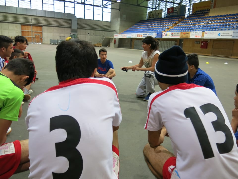 Jugendliche Asylsuchende in einer Sporthallte im Kreis mit der Sportlehrerin.