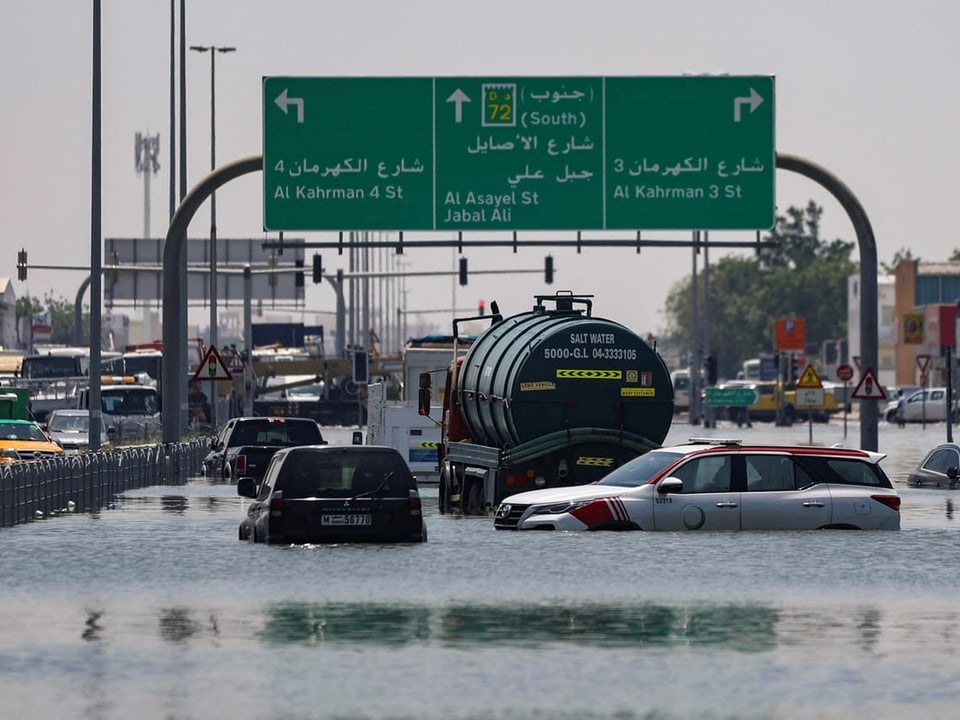 Überschwemmte Strasse mit Autos und Verkehrszeichen in einer Stadt.