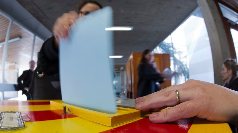 Gelb-rot gestreifte Abstimmungsurne. Eine Stimmbürgerin wirft einen Abstimmungszettel ein.