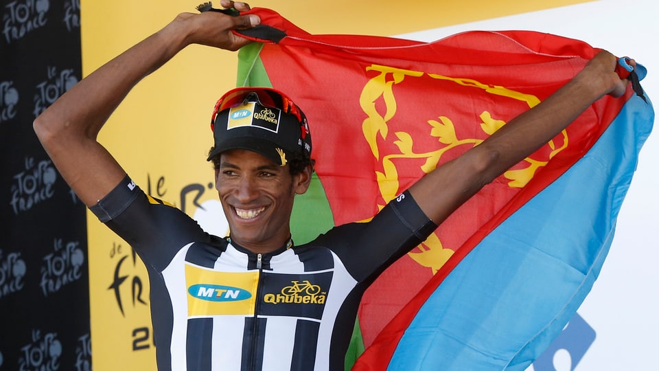 Daniel Teklehaimanot besteigt das Podium mit einer Eritrea-Flagge um seine Schultern.