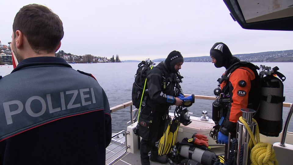 Zwei ausgerüstete Polizeitaucher an Deck ihres Bootes bei der Vorbereitung des Tauchgangs.