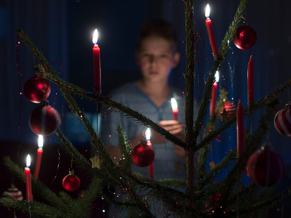 Knabe durch einen klassischen Weihnachtsbaum mit brennenden roten Kerzen und roten Kugeln fotografiert