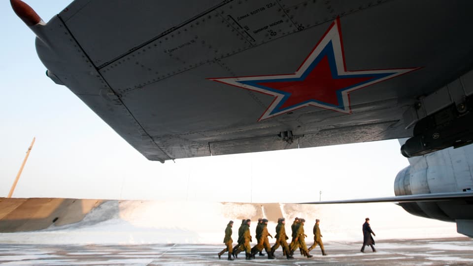 Soldaten marschieren unter einem Flugzeugflügel durch zu einer Transportmaschine