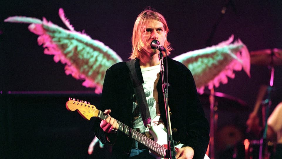 Kurt Cobain auf der Bühne. Hinter ihm sind Flügel, die auf seinem Rücken zu sein scheinen.
