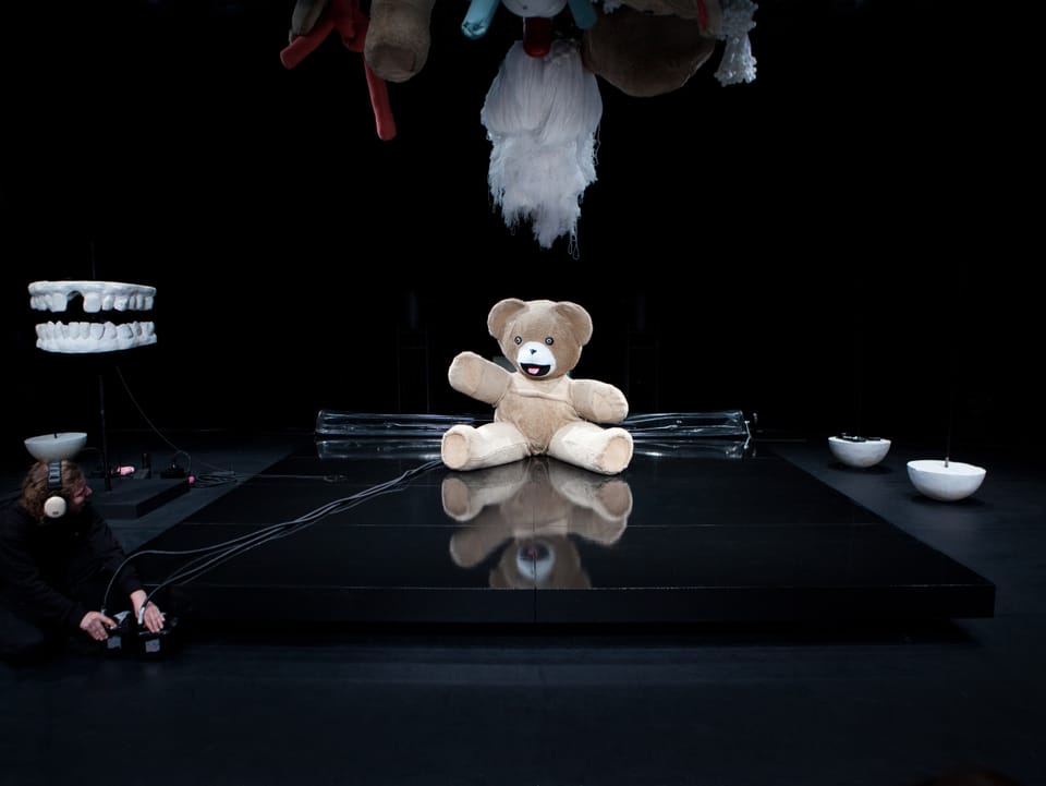 Ein überdimensionaler Teddybär sitzt auf einer Bühne.