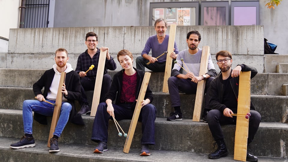 Sechs Musiker sitzen auf einer Treppe und halten Holzer und Klöppel in der Hand.