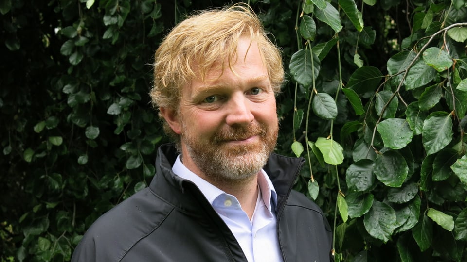 Portrait von einem Mann, der vor einer Pflanze steht.