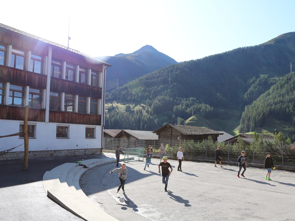 Kinder spielen auf dem Schulhausplatz, im Hintergrund ein Schulgebäude.