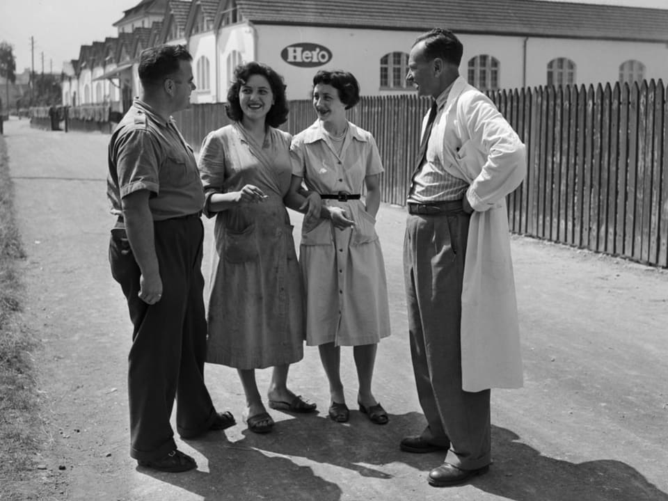 Schwarzweissbild: Zwei Frauen und zwei Männer im Gespräch vor einer Fabrik.