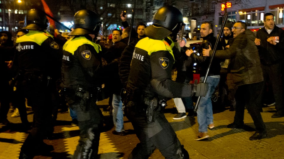 Polizisten mit Schlagstöcken vor Demonstranten.