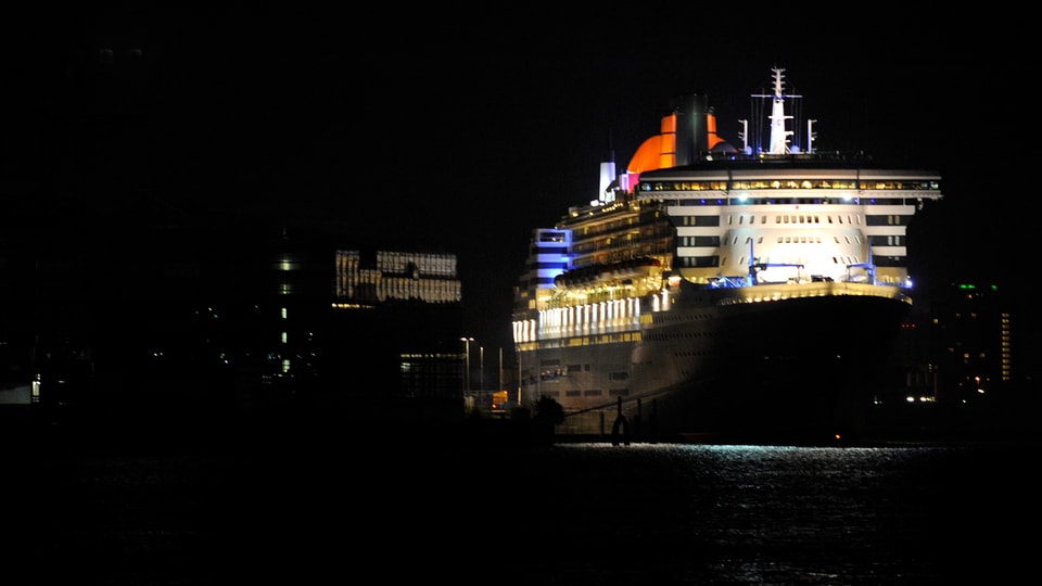 Queen Mary 2 in der Dunkelheit, Lichter beleuchten das Schiff.