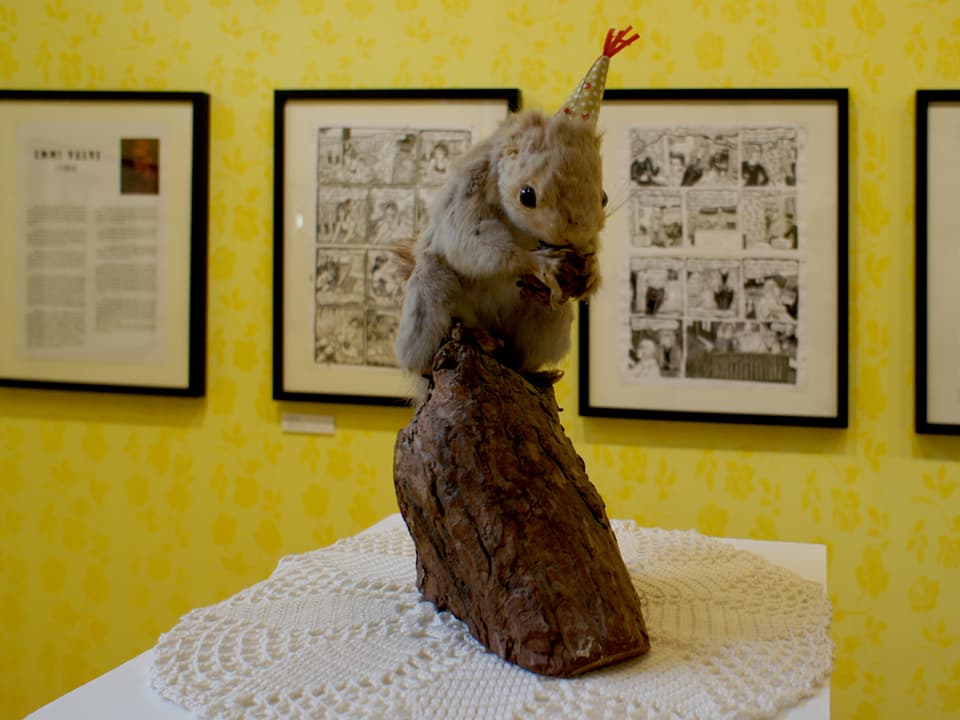 Ein ausgestopftes Eichhörnchen vor ausgestellten Comicsbildern.
