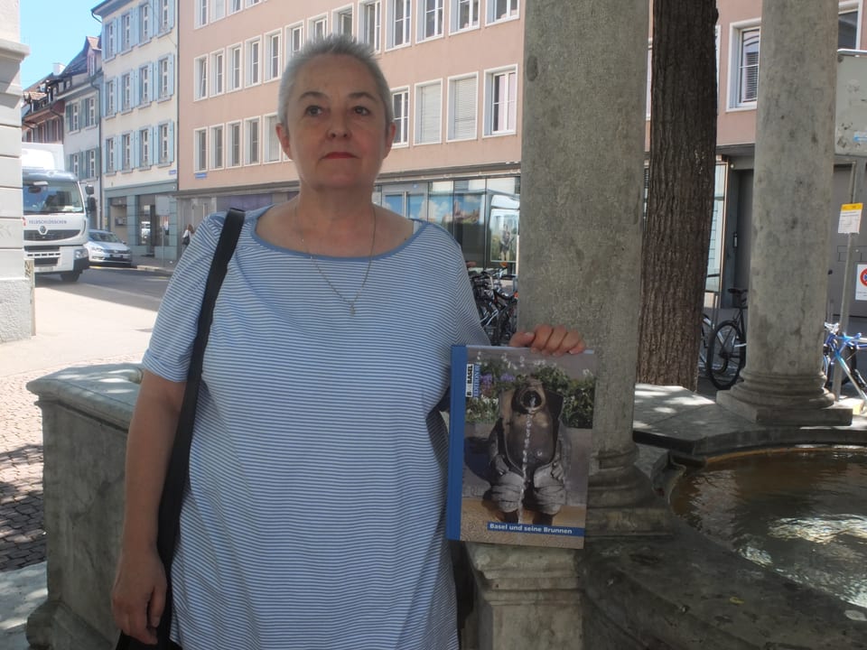 Christiane Widmer hält in der linken Hand ihr Buch über Basler Brunnen. Sie lehnt am Vierlinden-Brunnen. 