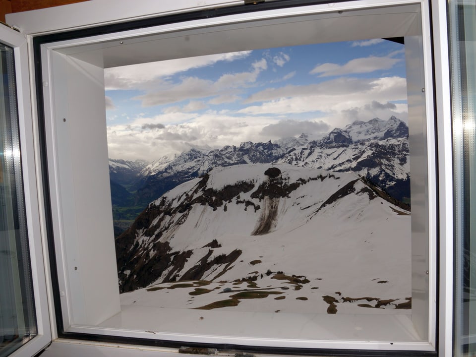 Ein offenes Fenster gibt den Blick auf ein Bergpanorama frei.