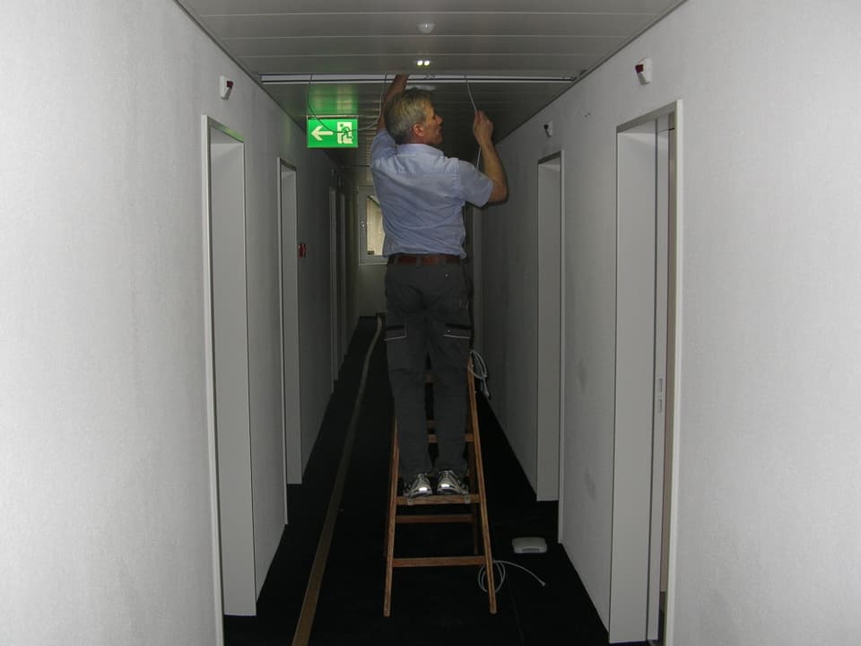 Handwerker im Gang vor Hotelzimmern auf einer Leiter stehend.