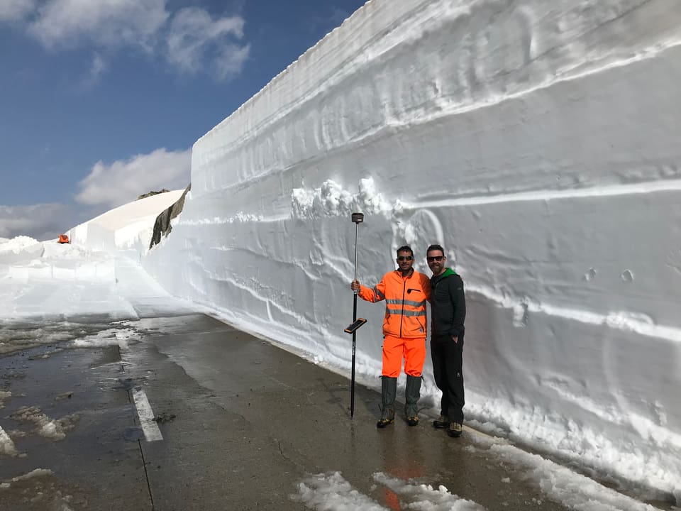 zwei Männer stehen vor einer fast dreimal so hohen Schneemauer.