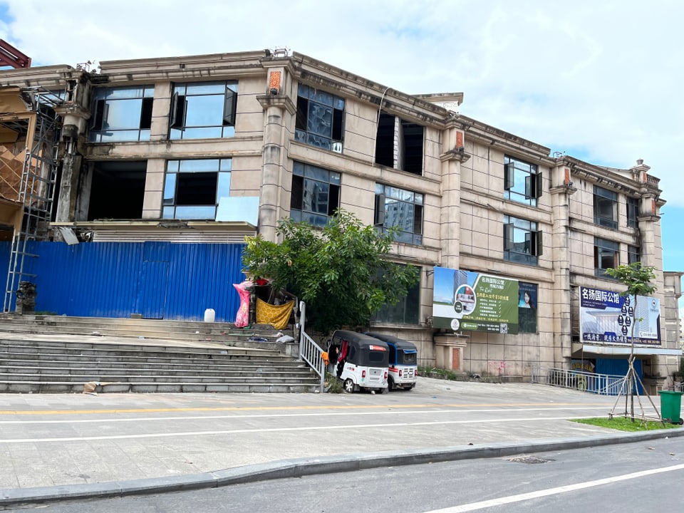 A three-story building stands on a street.  It has a pier.  Some windows are missing.