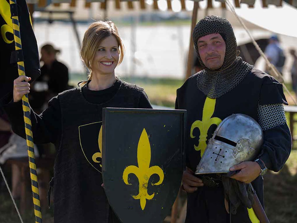 Mann und Frau in Ritterkleidung, Frau mit Schild und Banner, Mann mit Ritterhelm in der Hand
