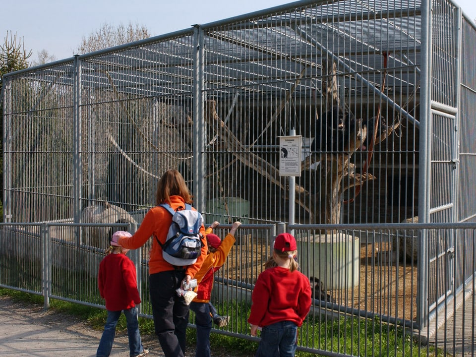 Eine Frau und drei Kinder stehen vor einem Käfig.