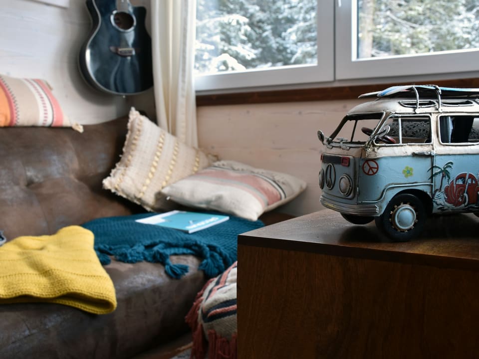 Blick in ein Wohnzimmer. Im Vordergrund ein Modell eines hellblauen, alten VW Bus