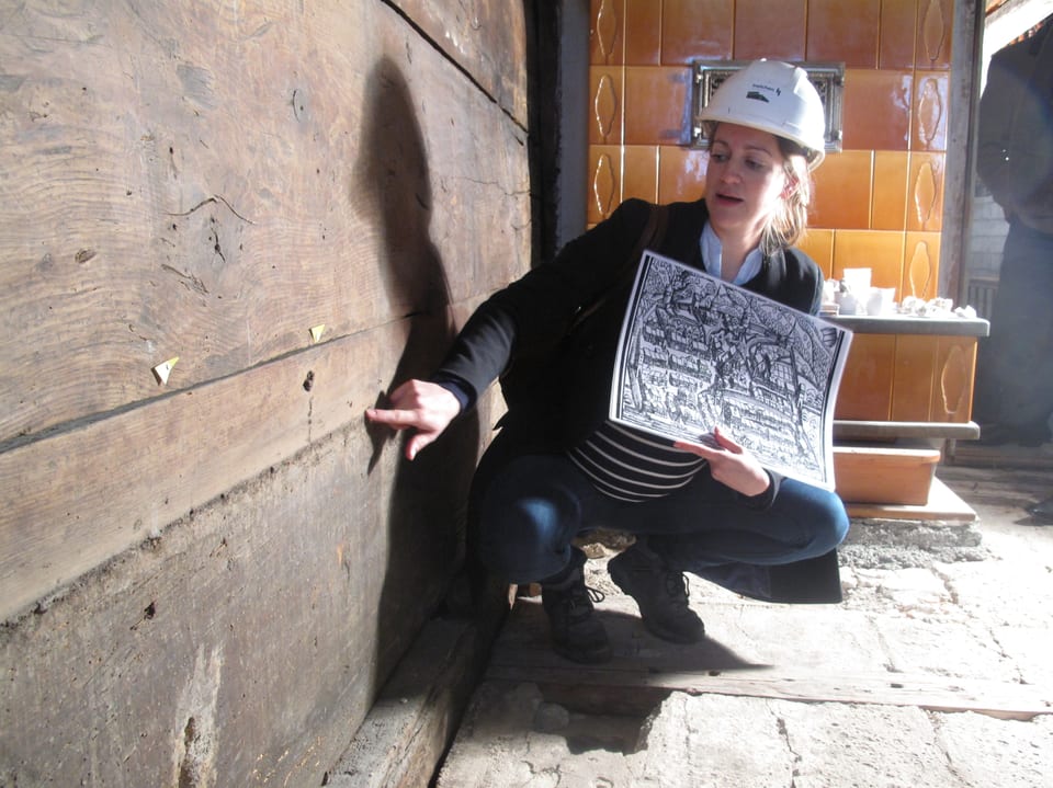 Eine Frau mit Helm zeigt auf eine Spalte in einer Holzwand.