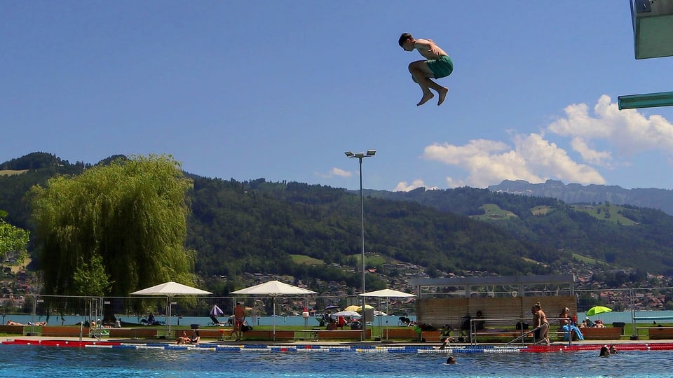 Jugendlicher springt vom Sprungturm ins Schwimmbecken.