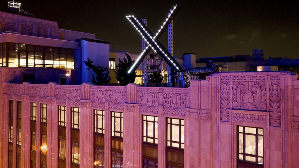 Nachansicht eine grossen «X» auf einem Gebäudedach mit leicht roter Beleuchtung. 