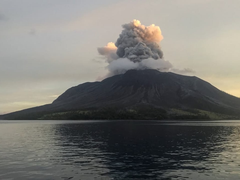 Vulkan bei einem Ausbruch über einem See bei Dämmerung.