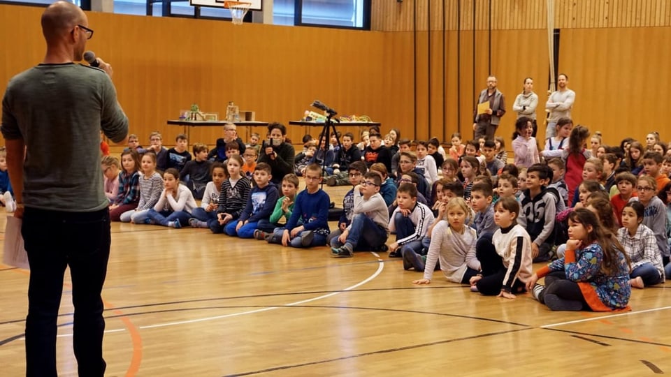 Kinder sitzen in einer Turnhalle