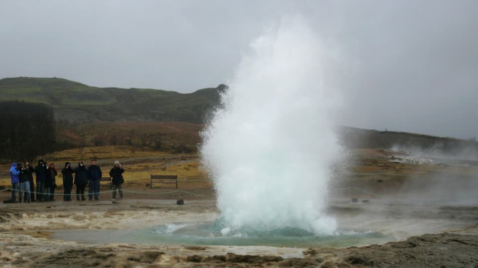 Touristen bestaunen eine heisse Quelle auf Island.