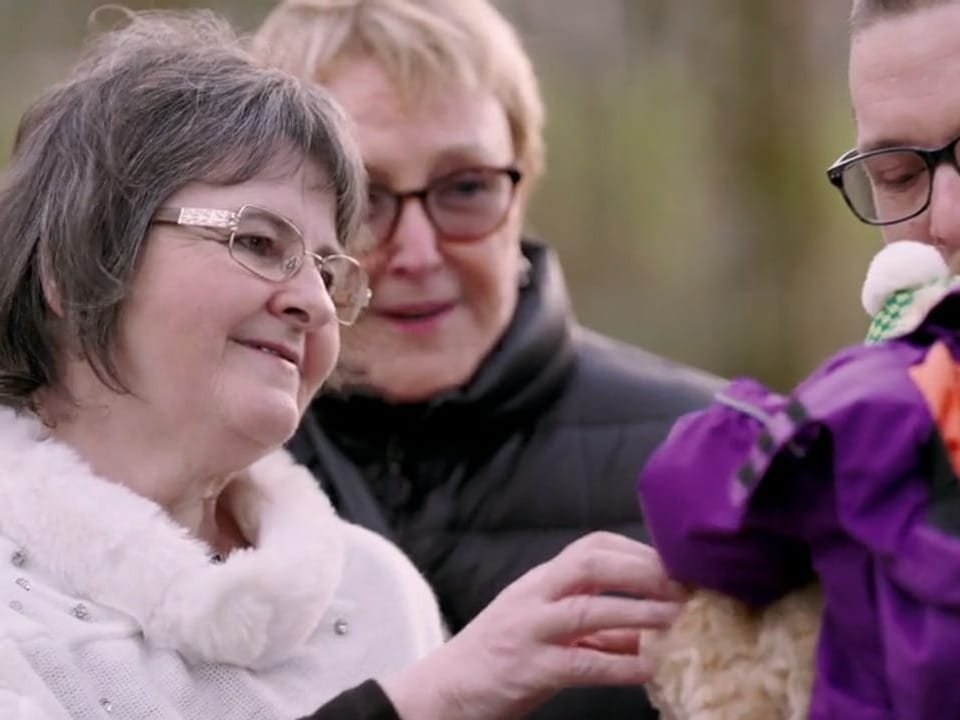 Ältere Frau mit Brille gibt einem Kind ein Teddybär.