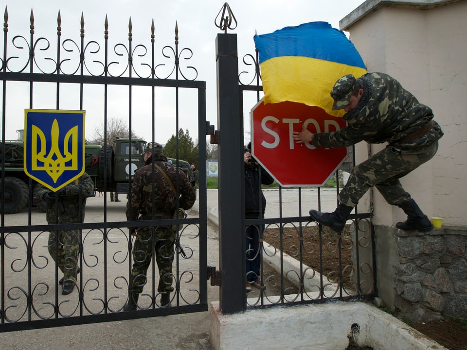 Soldat befestigt ukrainische Flagge an einem Kasernentor.