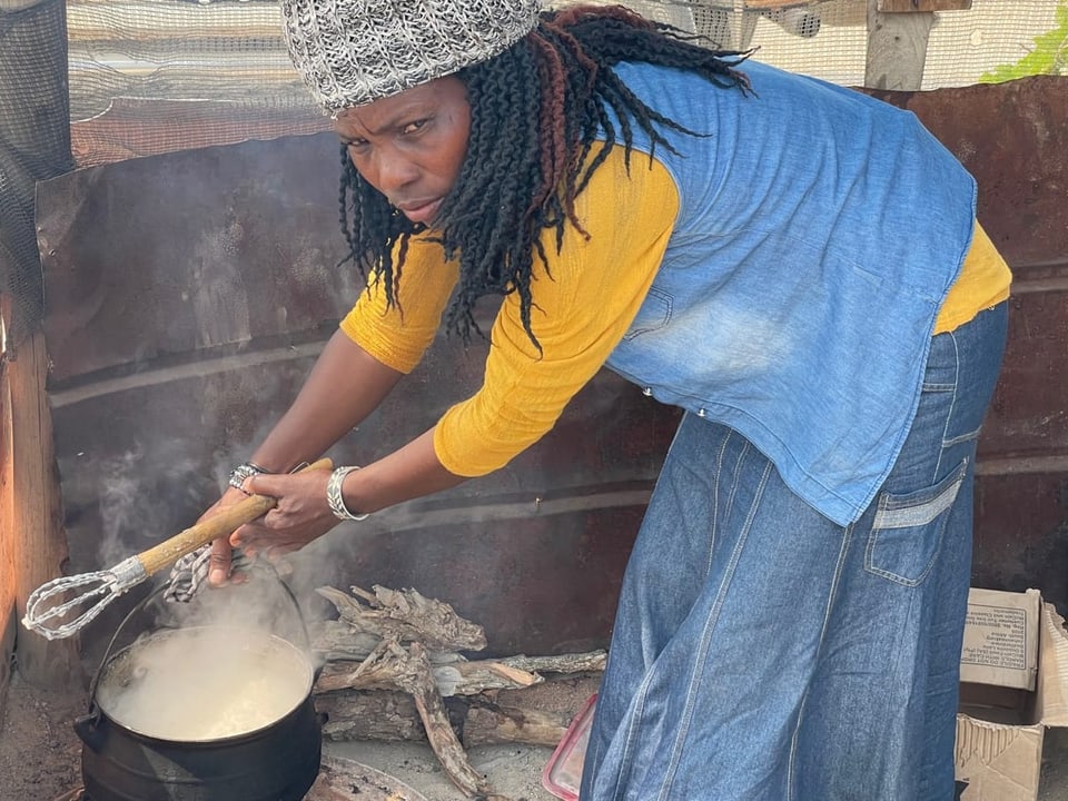 Karingo Herunga kocht Essen in einem Topf über dem Feuer.