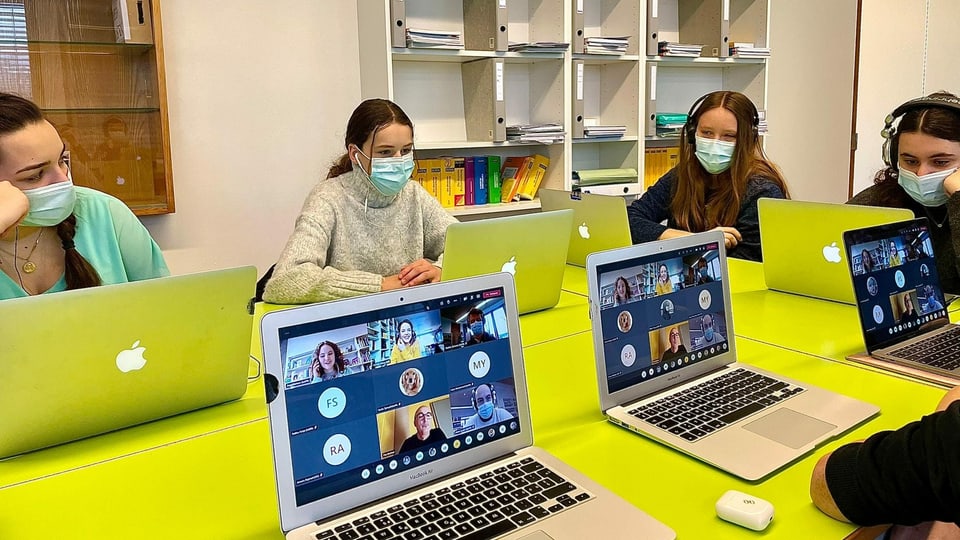 ... während ihre Klassenkameraden das Gespräch an ihren Laptops im Klassenzimmer verfolgen.