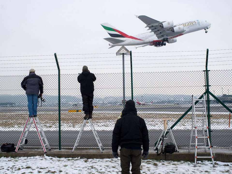 Fotografen am Zaun schauen startendem Flugzeug zu.