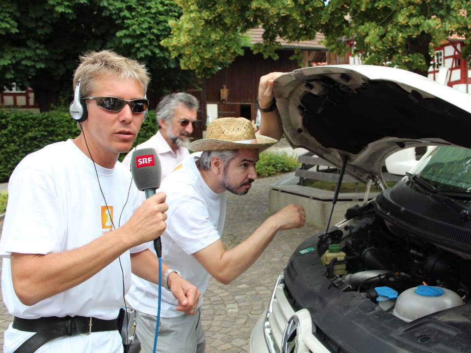 Reto Scherrer und Krispin Zimmermann vor der geöffneten Kühlerhaube des Reporterwagens.