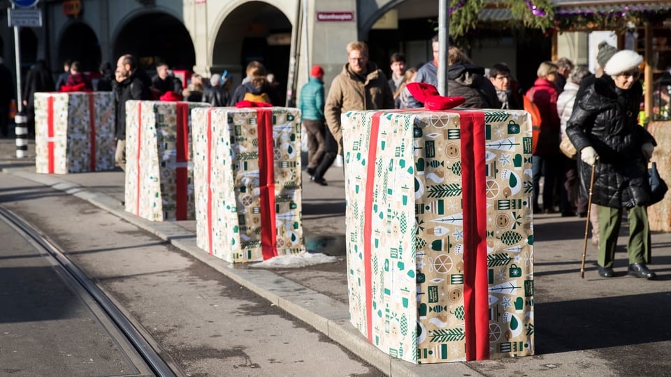 Als Geschenk verpackte Betonelemente stehen auf dem Trottoir. Eine alte Frau mit Stock geht daran vorbei.