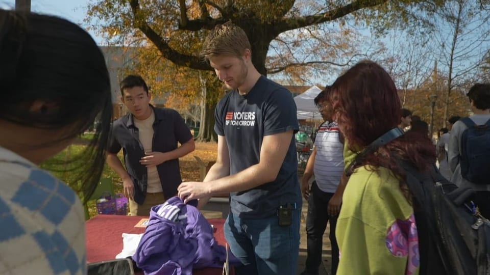 Um Putman stehen junge Menschen, während er etwas aus einem Rucksack auspackt.