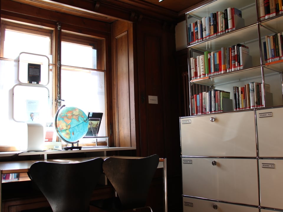 Globus auf einem Tisch am Fenster - daneben ein Büchergestell.