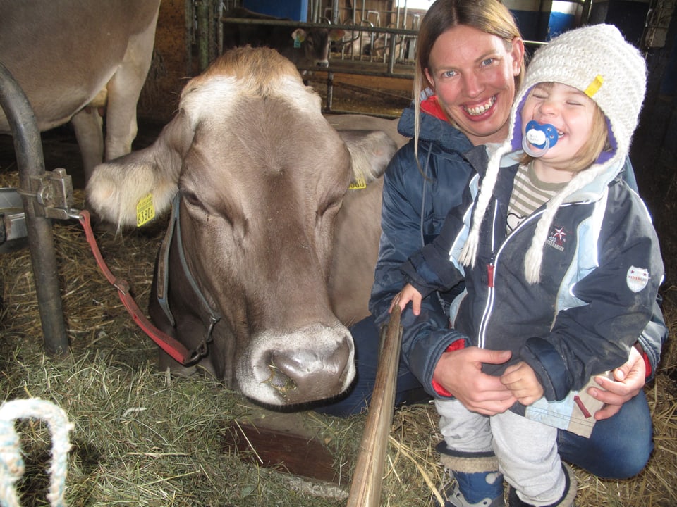 Eine Frau und ein kleines Mädchen stehen im Stroh neben einer Kuh.