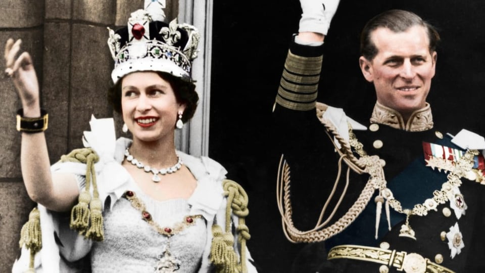 Links Frau in weissem Kleid und goldenen Kordeln, trägt Krone und winkt. Rechts winkt Mann in Uniform, lächelt.