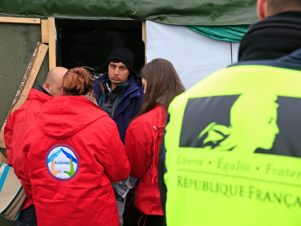 Menschen in roten Jacken sprechen mit einem Migranten