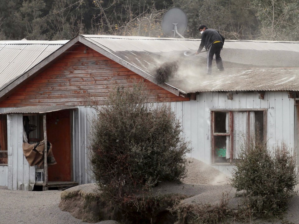 Ein Mann schaufelt das Dach seines Hauses von der Asche frei. 