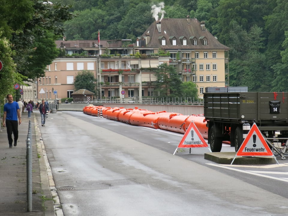 Passanten laufen auf einer Strasse, welche rechts durch rote Schläuche geschützt ist. 