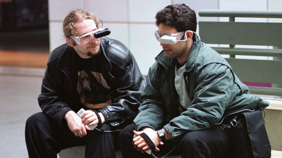 Thad Starner sitzt mit einem Kollegen in der Lobby des MIT. Beide tragen eine Computerbrille.