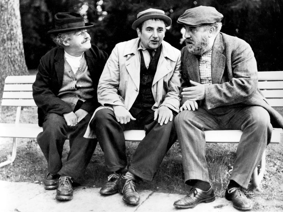 Drei Männer sitzen auf einer Bank und sprechen miteinander.