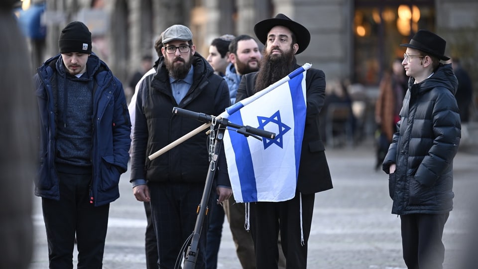 Orthodoxe Juden stehen mit einer israel-Flagge auf der Strasse.