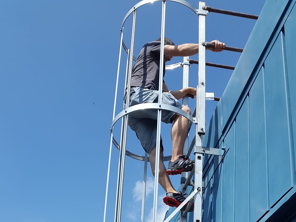 Mann kletter an Leiter auf ein Dach hinauf